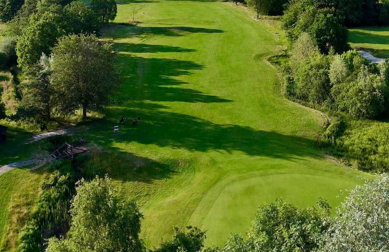 Luftaufnahme eines grünen Golfplatzes mit Bäumen und einem Abschlagbereich