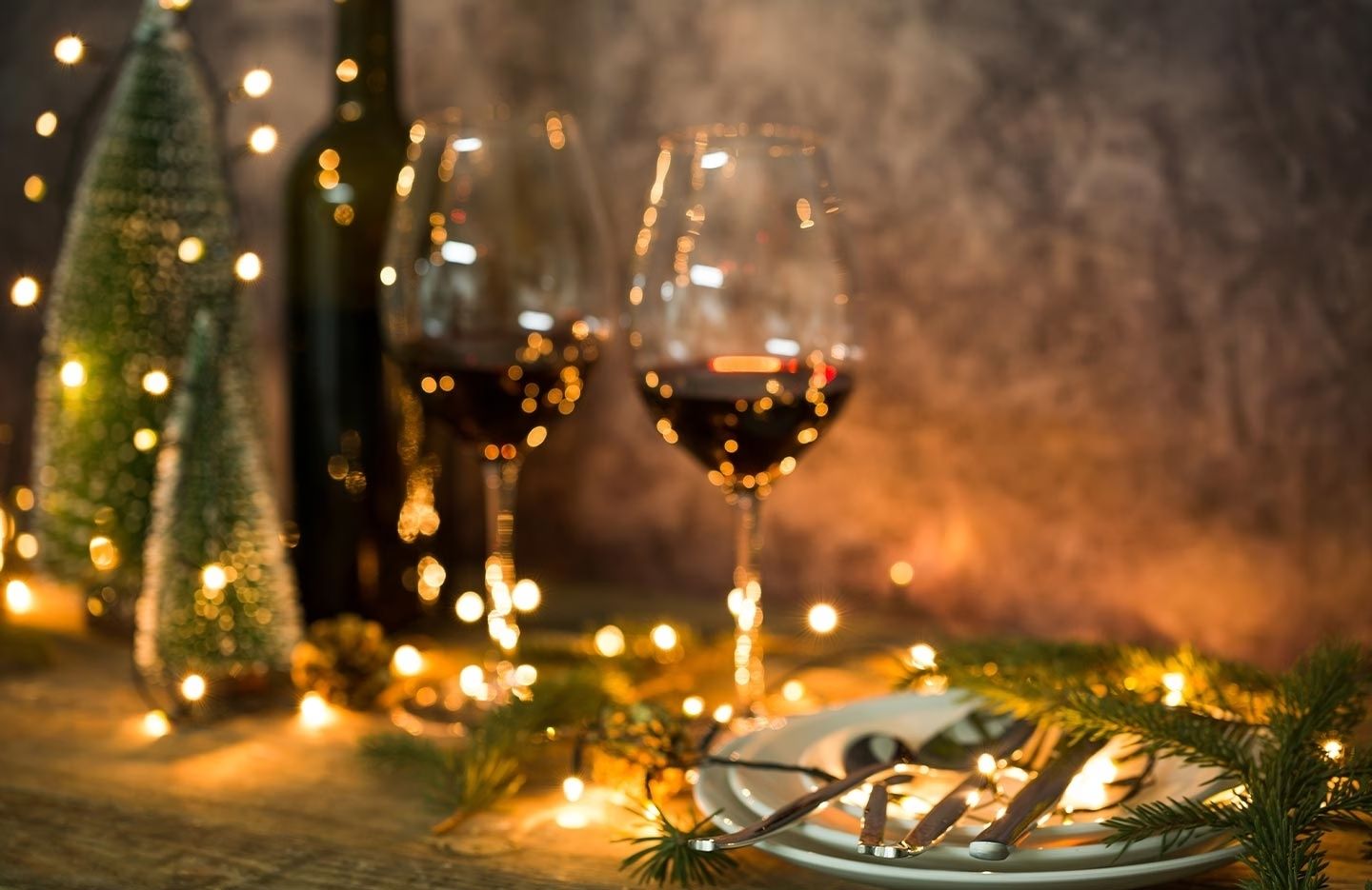 Weihnachtlich dekorierter Tisch mit zwei Weingläsern, Flaschen, Lichterkette und Tannenzweigen